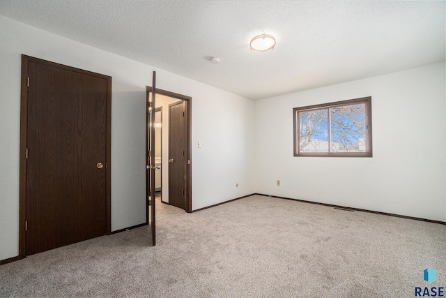 unfurnished bedroom with a textured ceiling, baseboards, and light colored carpet