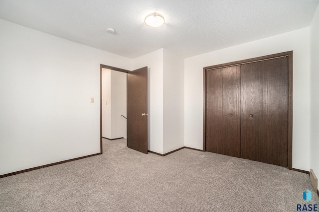 unfurnished bedroom with a closet, light colored carpet, a textured ceiling, and baseboards