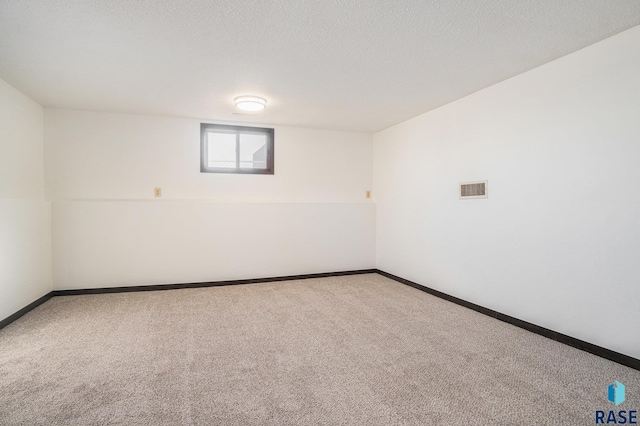 unfurnished room with carpet flooring, visible vents, baseboards, and a textured ceiling