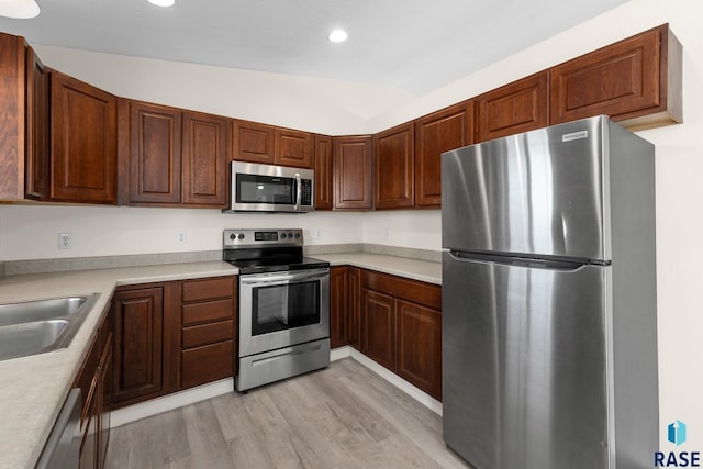 kitchen with appliances with stainless steel finishes, lofted ceiling, light wood-type flooring, and light countertops