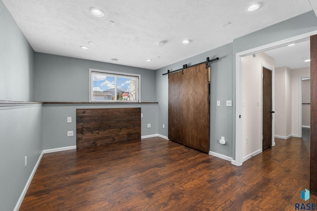 unfurnished living room featuring a barn door, baseboards, wood finished floors, a textured ceiling, and recessed lighting