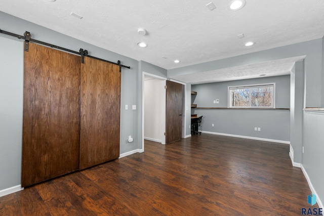 unfurnished bedroom with a barn door, a textured ceiling, baseboards, and wood finished floors