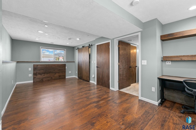 unfurnished office with a barn door, baseboards, wood finished floors, a textured ceiling, and recessed lighting