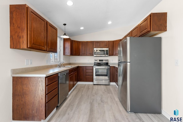 kitchen featuring light wood-style flooring, appliances with stainless steel finishes, vaulted ceiling, light countertops, and a sink