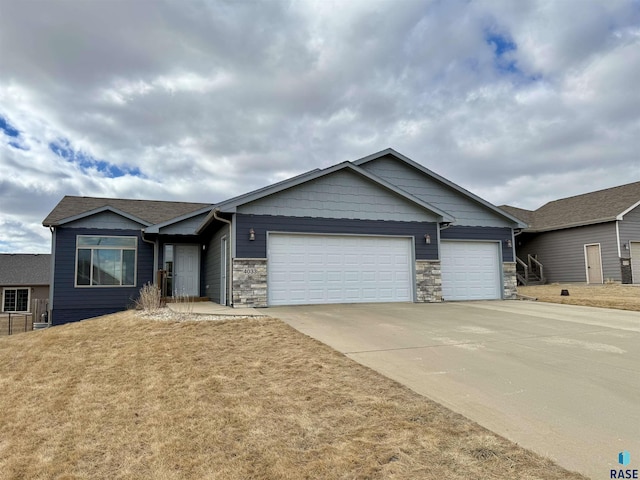 view of front of property with a front lawn, an attached garage, stone siding, and driveway