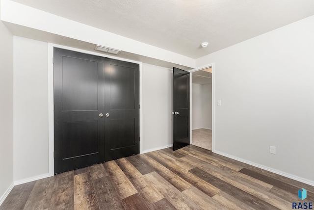 unfurnished bedroom featuring a closet, a textured ceiling, baseboards, and wood finished floors