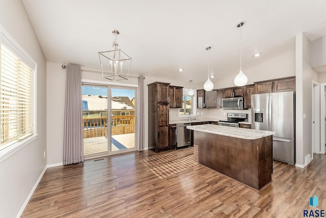 kitchen with dark brown cabinets, a kitchen island, vaulted ceiling, appliances with stainless steel finishes, and light wood-style floors