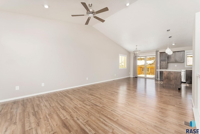 unfurnished living room with light wood-style flooring, ceiling fan with notable chandelier, baseboards, and vaulted ceiling