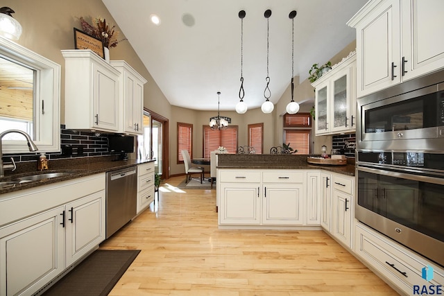 kitchen featuring tasteful backsplash, appliances with stainless steel finishes, a sink, a chandelier, and a peninsula