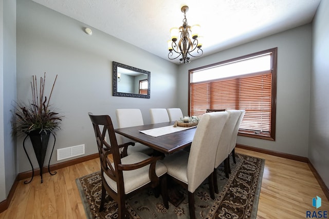 dining area featuring baseboards, light wood-style flooring, visible vents, and a notable chandelier