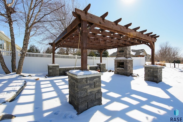 snow covered patio featuring an outdoor stone fireplace, a fenced backyard, and a pergola