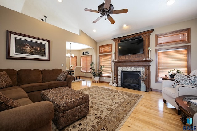 living room featuring lofted ceiling, ceiling fan with notable chandelier, a fireplace, baseboards, and light wood-type flooring