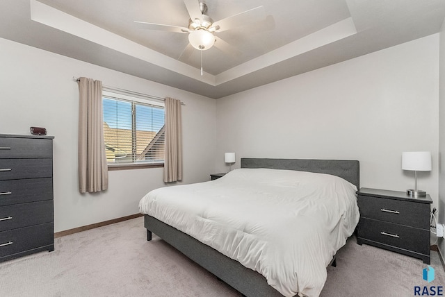 bedroom featuring ceiling fan, a tray ceiling, light colored carpet, and baseboards