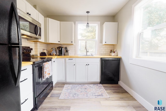 kitchen with a sink, baseboards, light wood-type flooring, black appliances, and tasteful backsplash