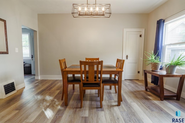 dining space with light wood-style floors, baseboards, visible vents, and a notable chandelier