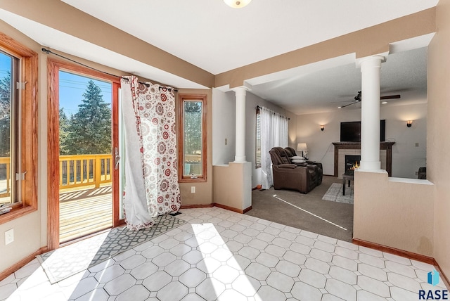 interior space featuring a warm lit fireplace, ornate columns, ceiling fan, and baseboards