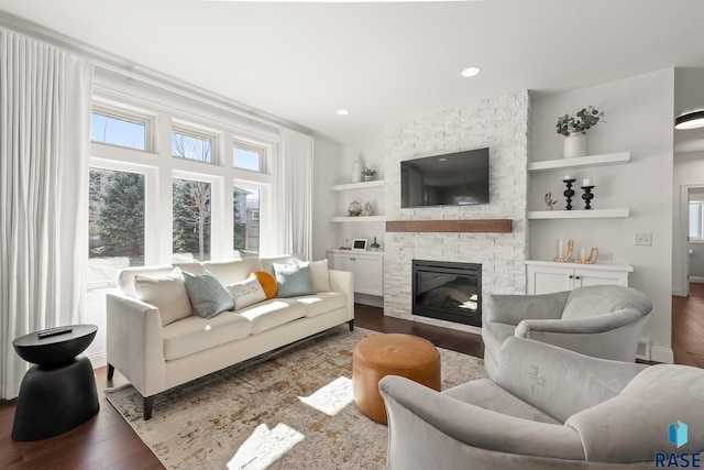 living room with recessed lighting, built in features, dark wood-type flooring, and a stone fireplace