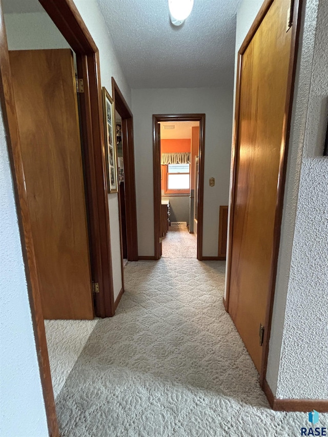 corridor featuring light carpet, a textured ceiling, and baseboards