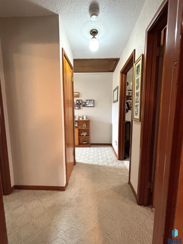 hallway with a textured ceiling, carpet, and baseboards