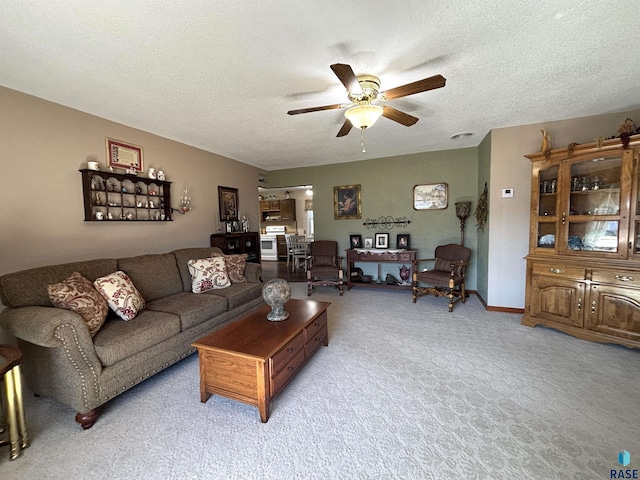 living area featuring light carpet, ceiling fan, baseboards, and a textured ceiling