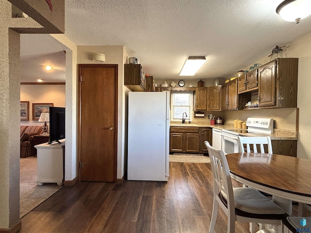 kitchen with a textured ceiling, white appliances, dark wood-type flooring, a sink, and light countertops