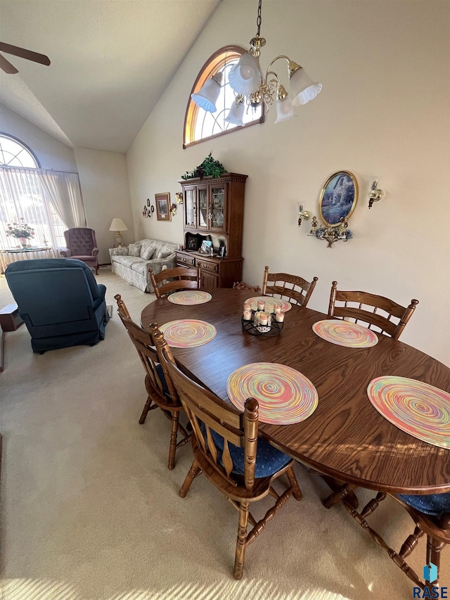 dining area with ceiling fan with notable chandelier, high vaulted ceiling, and carpet