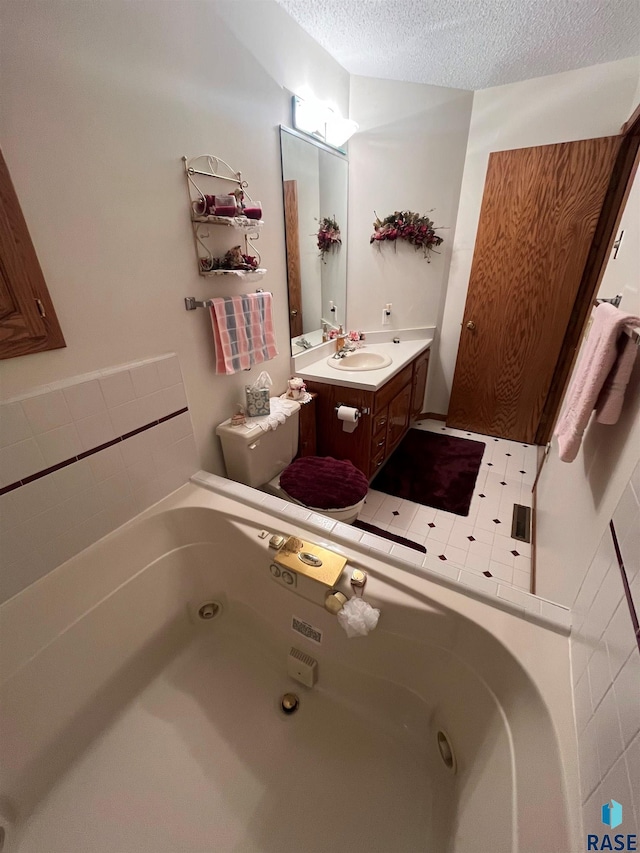 full bath featuring a jetted tub, toilet, a textured ceiling, and vanity