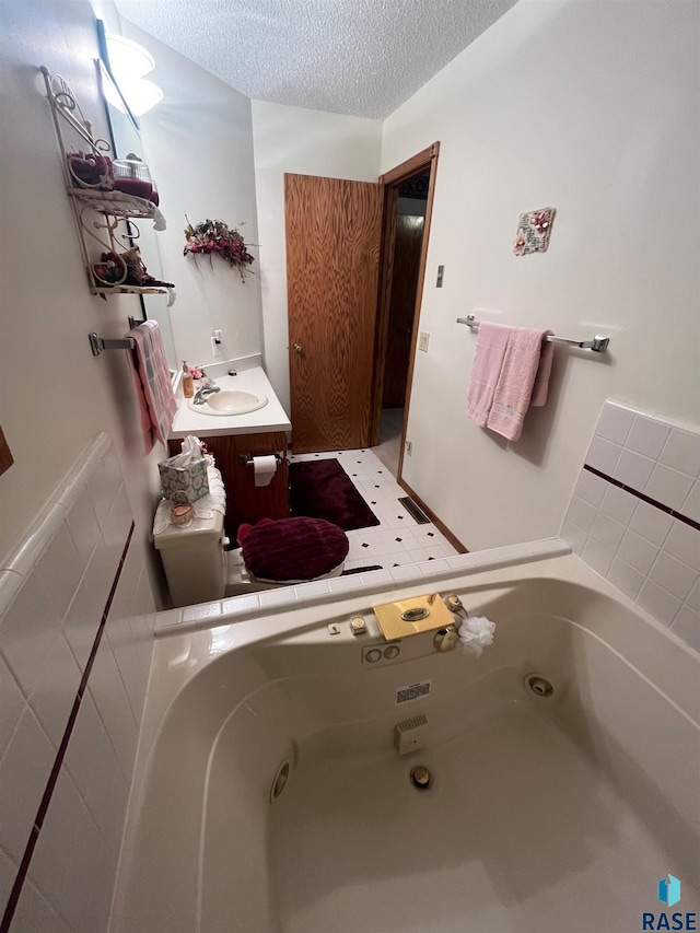 full bath with a tub with jets, a textured ceiling, and vanity