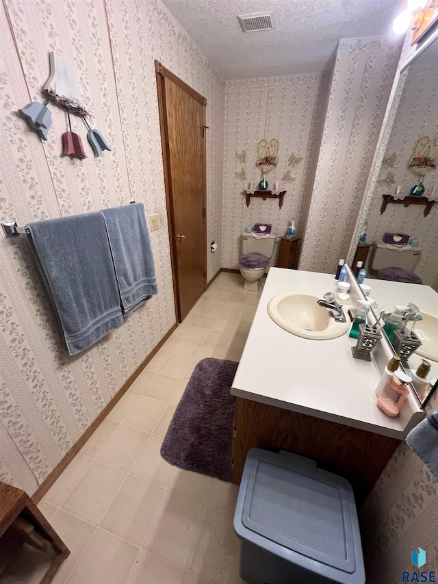 bathroom with a textured ceiling, visible vents, baseboards, tile patterned floors, and wallpapered walls