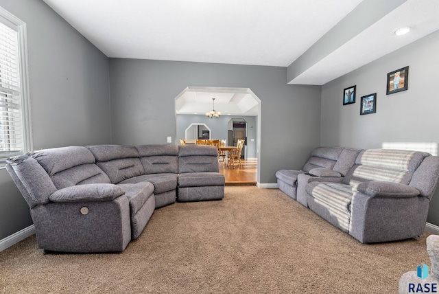 living room with arched walkways, carpet, baseboards, and a notable chandelier