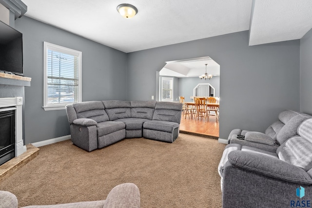 carpeted living area with arched walkways, a fireplace, a notable chandelier, and baseboards