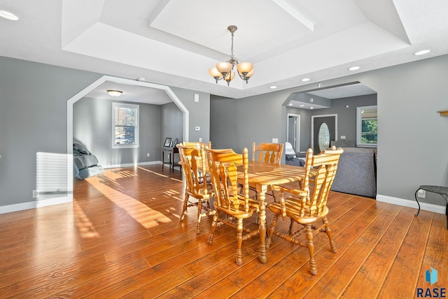 dining room with hardwood / wood-style flooring, baseboards, a tray ceiling, and a chandelier