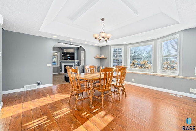 dining space with visible vents, a fireplace, a tray ceiling, and baseboards