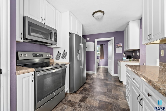 kitchen with baseboards, white cabinets, stone finish flooring, stainless steel appliances, and light countertops