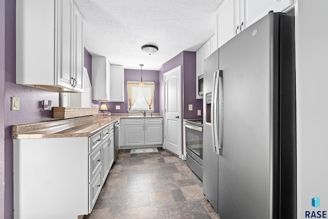 kitchen featuring white cabinets, decorative light fixtures, stone finish flooring, stainless steel appliances, and a sink