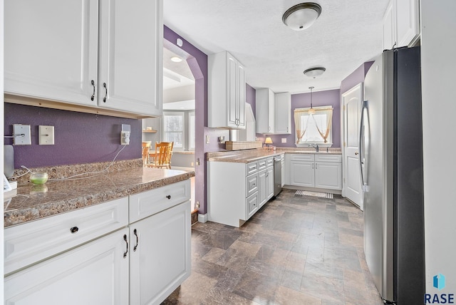 kitchen with appliances with stainless steel finishes, stone finish flooring, a textured ceiling, white cabinetry, and a sink