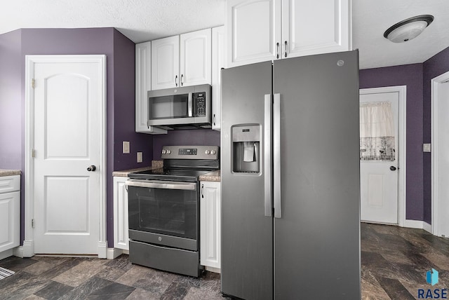 kitchen with baseboards, appliances with stainless steel finishes, stone finish flooring, light countertops, and white cabinetry