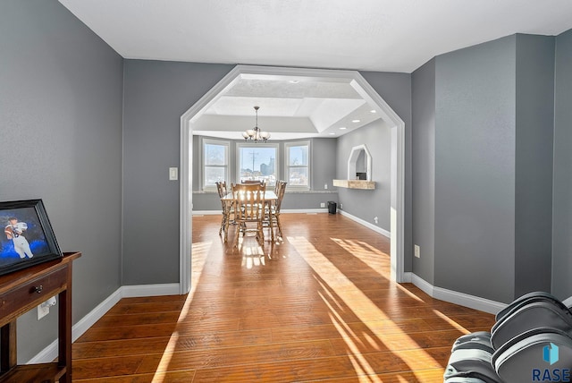 dining area with a chandelier, a raised ceiling, baseboards, and wood finished floors