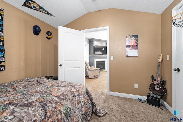 bedroom featuring baseboards, a glass covered fireplace, carpet, vaulted ceiling, and a textured ceiling