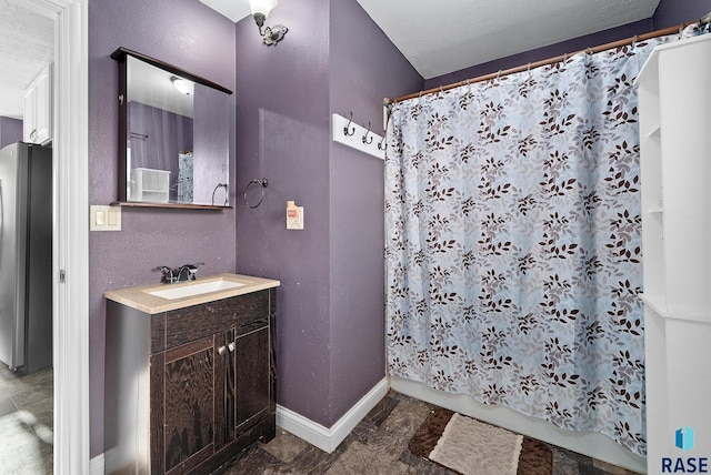 full bathroom with a textured wall, baseboards, and vanity