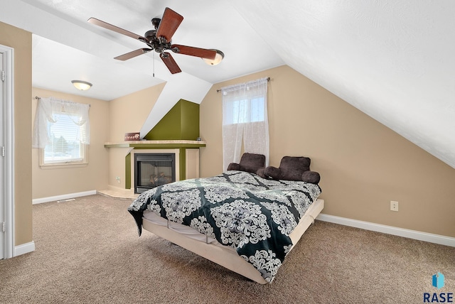 bedroom featuring a glass covered fireplace, carpet flooring, vaulted ceiling, ceiling fan, and baseboards