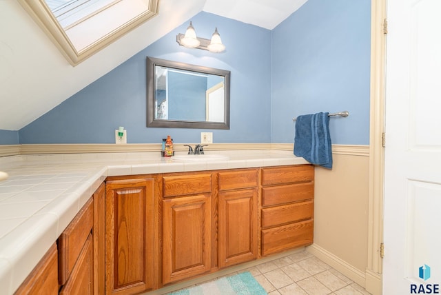 bathroom with vaulted ceiling with skylight, vanity, and tile patterned floors