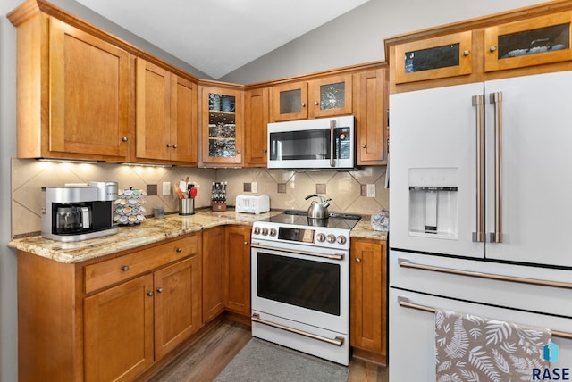 kitchen with light stone counters, decorative backsplash, vaulted ceiling, wood finished floors, and white appliances