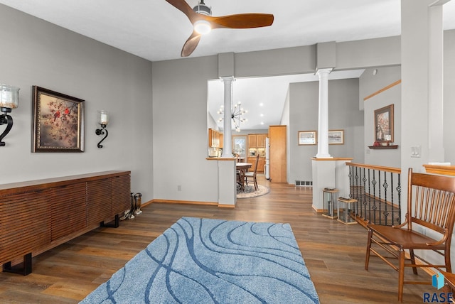 sitting room featuring ceiling fan with notable chandelier, wood finished floors, visible vents, baseboards, and ornate columns