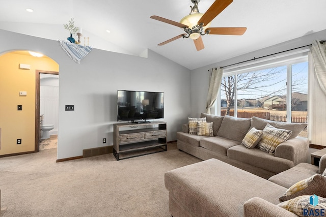 living area with arched walkways, light carpet, vaulted ceiling, ceiling fan, and baseboards