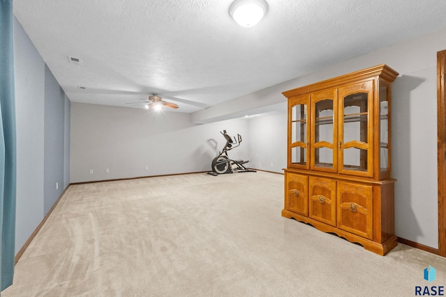 interior space featuring a textured ceiling, ceiling fan, light colored carpet, visible vents, and baseboards