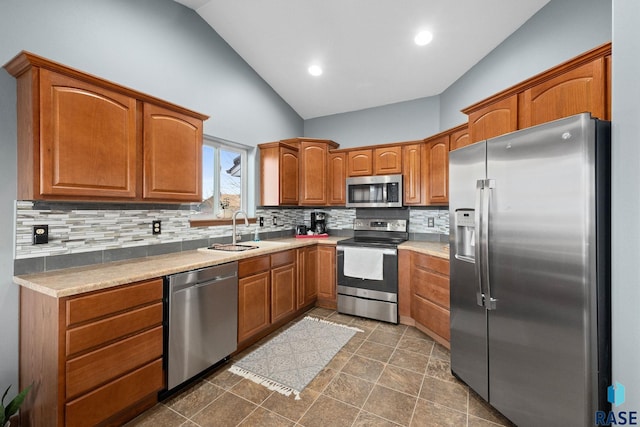 kitchen with a sink, vaulted ceiling, appliances with stainless steel finishes, tasteful backsplash, and brown cabinetry