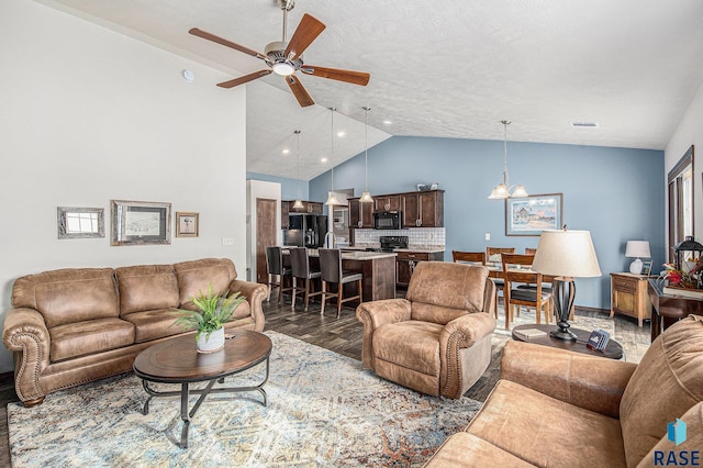 living room featuring visible vents, lofted ceiling, wood finished floors, and ceiling fan with notable chandelier