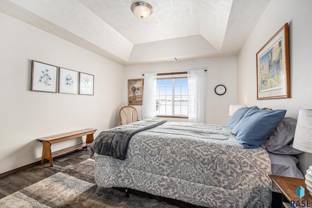 bedroom featuring visible vents, a tray ceiling, a textured ceiling, wood finished floors, and baseboards