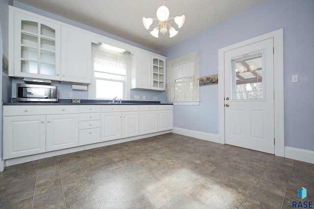 kitchen with glass insert cabinets, dark countertops, white cabinets, and stainless steel microwave